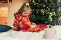 A little girl opens a Christmas present near the Christmas tree. Christmas time, gifts, festive mood. The concept of Royalty Free Stock Photo