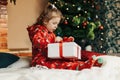 A little girl opens a Christmas present near the Christmas tree. Christmas time, gifts, festive mood. The concept of Royalty Free Stock Photo