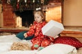 A little girl opens a Christmas present near the Christmas tree. Christmas time, gifts, festive mood. The concept of Royalty Free Stock Photo