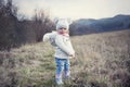 A little girl is outside with her pet. Cute baby girl wearing a ferret in a hood. The child and his living furry pet