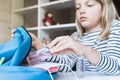 Little girl packing blue backpack in kids`s room. Face mask, bottle of sanitizer, stationery, pens, multicolored markers,