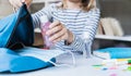 Little girl packing blue backpack in kids`s room. Face mask, bottle of sanitizer, stationery, pens, multicolored markers,