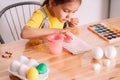Little girl painting artificial eggs for Easter at a large wooden table