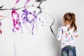 Little girl painting a white wall with colorful paint. Royalty Free Stock Photo