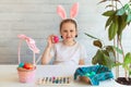 Little Girl paints eggs for Easter Holiday Baby Wears Rabbit ears on Easter Day.