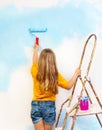 Little girl paints the wall standing on a ladder