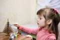 A little girl paints a wooden toy in the shape of a Christmas tree. Children\'s leisure Royalty Free Stock Photo