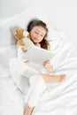 Little girl in pajamas using digital tablet while lying in bed Royalty Free Stock Photo