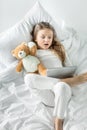 Little girl in pajamas using digital tablet while lying in bed Royalty Free Stock Photo