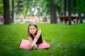 A little girl in the park is doing yoga stretching leaning on her leg. A girl is sitting on a twine