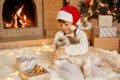 Little girl with Pekingese dog posing in holiday room, sitting on floor on soft carpet near fireplace and fir tree with her Royalty Free Stock Photo