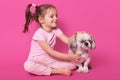 Little girl pets her pekingese while sitting with crossed legs on floor. Adorable child likes her pet. Cute smiling kid looks at