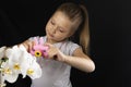 Little girl photographs a white orchid flower with a pink camera in the studio on a dark background Royalty Free Stock Photo