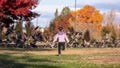 Little girl in a pick jacket and black jeans chasing geese sitting on a field in a park