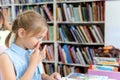 Little girl picking her nose,reading book with fairy tales in children`s library. Special reading kids room. Many shelves with Royalty Free Stock Photo