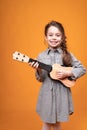 Little girl in pigtails are holding a small guitar in their hands while standing on a bright background Royalty Free Stock Photo