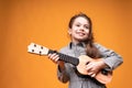 Little girl in pigtails are holding a small guitar in their hands while standing on a bright background Royalty Free Stock Photo