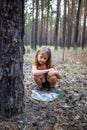 Little girl in the pine forest near the plastic bottle.