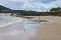 Little girl in pink bathing suit running toward ocean as sea gulls stand around and she is reflected in water on beach - other peo Royalty Free Stock Photo