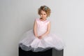 A little girl in a pink dress and crown sits on a black cube on a white background Royalty Free Stock Photo