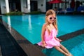 Little girl in pink dress and funny sunglasses sits by poolside. Child enjoys sunny day at outdoor swimming pool, summer Royalty Free Stock Photo