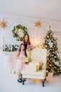 Little girl in pink dress with her mother standing near the armchair by the Christmas tree in the New Year`s room Royalty Free Stock Photo