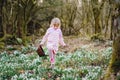 Little girl in pink dress making egg hunt in spring forest on sunny day, outdoors. Cute happy child with lots of