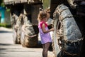 A little girl in a pink dress next to the big wheels of a car in chains.