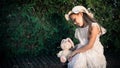 Little girl in a pink dress and panama with a soft rabbit toy portrait on a foliage background