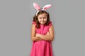 Little girl in a pink dress with polka dots on a gray background. Child in Easter bunny ears angry with crossed arms