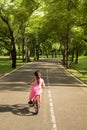 The little girl in pink dress trying to ride a bike headed for a narrow street in the park.