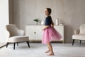 Little girl in pink fluffy skirt standing in living room