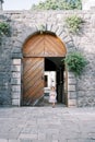 Little girl with a pink rabbit comes out of the arched wooden doors into the courtyard of an ancient castle