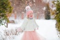 Little girl in a pink skirt in winter smiles in the park and throws up the snow Royalty Free Stock Photo