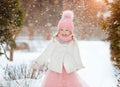 Little girl in a pink skirt in winter smiles in the park and throws up the snow Royalty Free Stock Photo