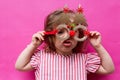 A little girl in a pink striped dress with Christmas tree-shaped glasses. The girl's very surprised festive face