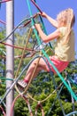 A little girl on the playground climbs the ropes while walking.