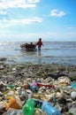 Haiti - March, 2017: A little girl playing in the dirty ocean with a old fish boat at a really polluted beach by plastic waste and