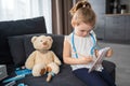 Little girl playing doctor with toys and teddy bear on the sofa in living room at home Royalty Free Stock Photo