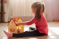 Little girl playing with her doll house. Child sitting on floor in her bedroom, female kid plays in her room at home or Royalty Free Stock Photo