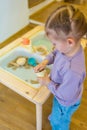 Little girl playing with kinetic sand and wooden toys. Sensory development and experiences, themed activities with Royalty Free Stock Photo