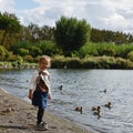 Little girl playing on the lakeshore with the ducks. Childhood concept. Life outdoors concept