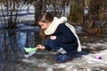 A little girl playing with paper boats in early spring semi-frozen puddles