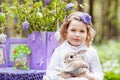 Little girl  playing with real rabbit in the garden. Laughing child at Easter egg hunt with  pet bunny. Spring outdoor fun for Royalty Free Stock Photo