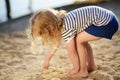 Little girl playing with sand during walk by the lake at summer day. Baby draw finger on sand Royalty Free Stock Photo