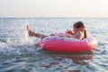 Little girl playing in the sea. A child girl raises her legs up in the water and splashes water drops