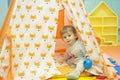 Little girl playing in a tent with red fox print. Toddler playing hide and seek in a toy house. Light and bright playroom.