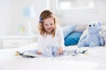 Little girl playing with toy and reading a book in bed Royalty Free Stock Photo