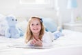 Little girl playing with toy and reading a book in bed Royalty Free Stock Photo