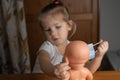 a little girl plays with a baby doll at home, puts a medical mask on a doll. focus on the doll, child in blur